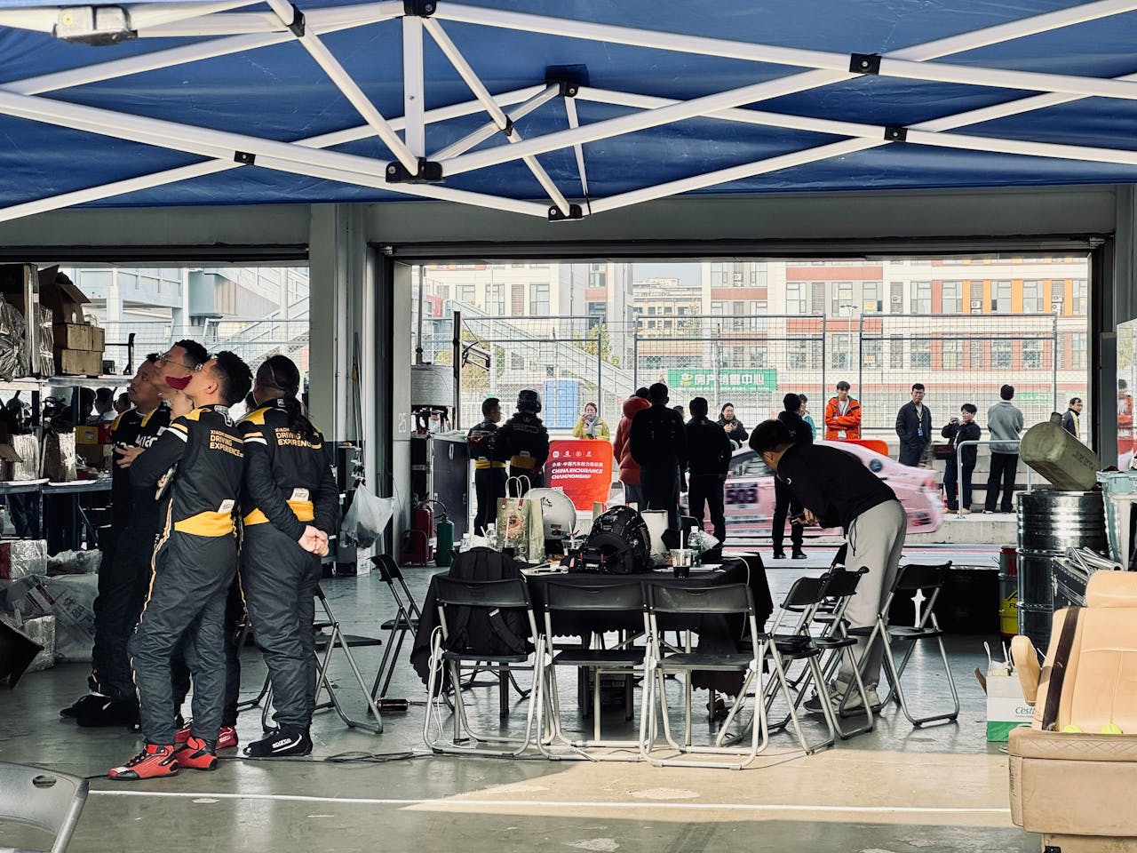 A racing team preps in a pit garage while cars zoom past outside, highlighting teamwork and focus.